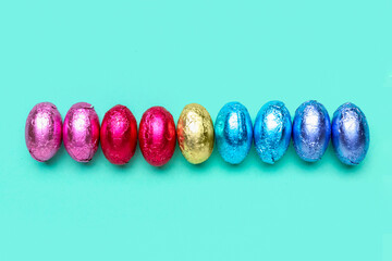 Row of chocolate Easter eggs in foil on color background
