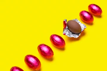 Fototapeten Unpacked chocolate Easter egg among wrapped ones on yellow background, closeup © Pixel-Shot