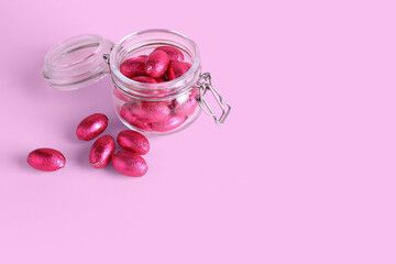 Glass jar of chocolate Easter eggs on pink background