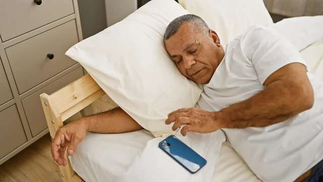 A middle-aged hispanic man sleeping in a bedroom with a smartphone by his side.