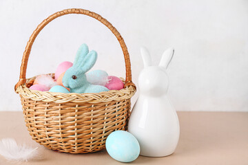 Basket with Easter eggs and bunnies on beige table against white background