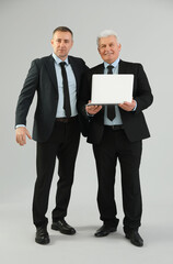 Mature brothers in suits with laptop on grey background