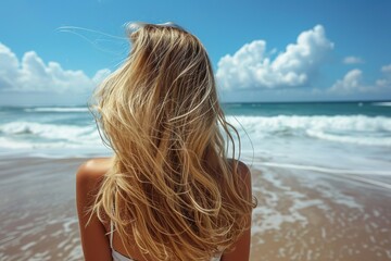 Fototapeta na wymiar An attractive young blond woman with beautiful long hair on a sandy beach in the . back view.
