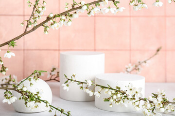 Podiums with blooming branches on table near beige tile wall. Hello spring