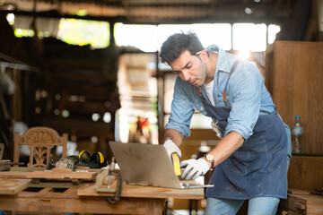 Carpenter working on laptop in his workshop at a woodworking factory
