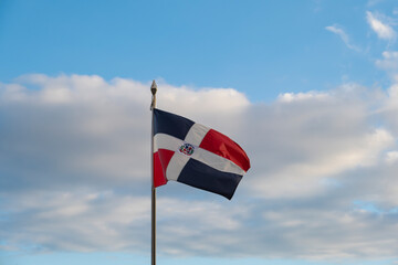Dominican Republic flag on a mast waiving against blue sky and white clouds background. Shot in historical center of Santo Domingo city.