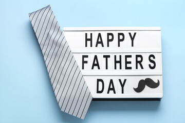 Board with text HAPPY FATHER'S DAY, paper mustache and necktie on blue background
