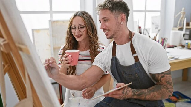Man and woman artists collaborate in a bright studio, painting, sipping coffee, and discussing art.