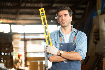 Portrait of a carpenter holding a spirit level in his workshop.