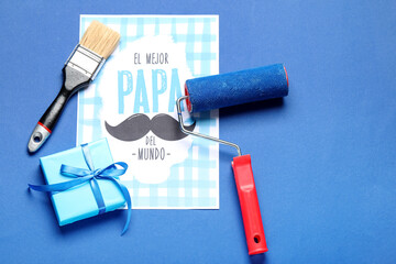 Card for Father's Day with gift, paint roller and brush on blue background