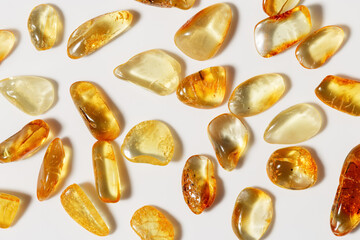 Amber stones at sunlight on light background, stone yellow beige color. Natural gemstone mineral material, healing crystal. Top view Amber texture. Nature gems, pieces ancient resin.