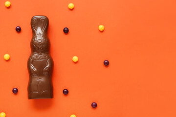 Chocolate Easter bunny and candies on orange background