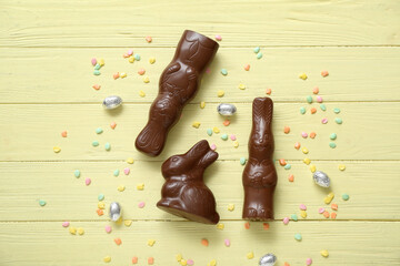 Chocolate bunnies, Easter eggs in foil and sprinkles on yellow wooden background