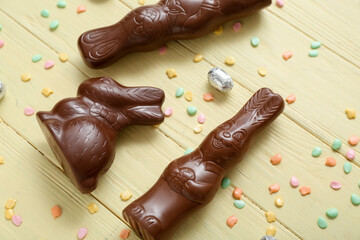 Chocolate bunnies, Easter egg in foil and sprinkles on yellow wooden background