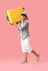 Young man with suitcase on pink background