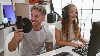 A man and a woman, both musicians and singers, collaborate joyfully in a modern music studio with recording equipment.