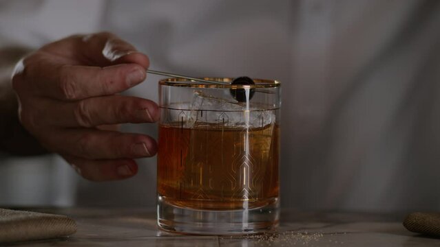 Bartender garnishes an old fashioned with a maraschino cherry