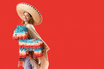Pretty young woman in sombrero and poncho with pinata on red background