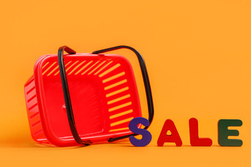 Small red shopping basket with text SALE on orange background, closeup