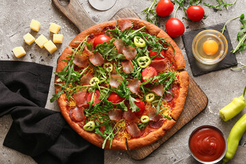 Wooden board of delicious pizza with tomatoes and arugula on grey background