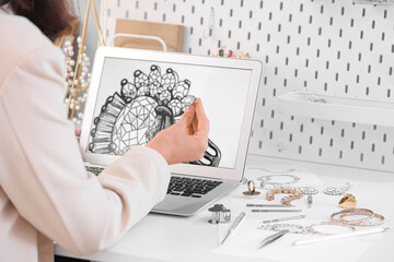 Female jewelry designer working with laptop and sketch of ring in office