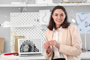 Happy female jewelry designer with laptop and tools working in office
