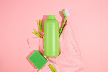 Against a pink background and pink wipe, green bottle of detergent with scrub sponges, brush and...