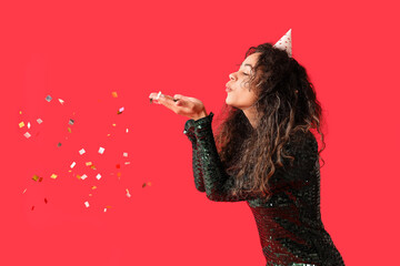 Beautiful young African-American woman in party hat with confetti celebrating Birthday on red background