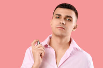 Young man applying perfume on pink background, closeup