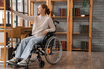 Young redhead woman in wheelchair taking book from shelf at library