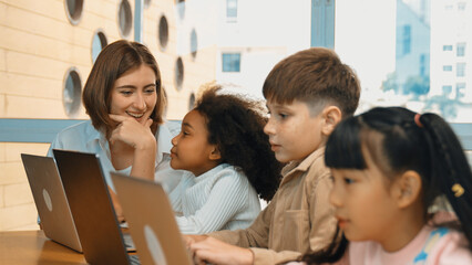 Smart teacher teaching and looking student using laptop at classroom. Professional instructor...