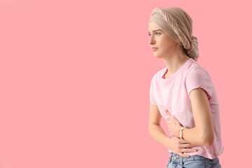 Young woman after chemotherapy suffering from pain on pink background. Stomach cancer concept