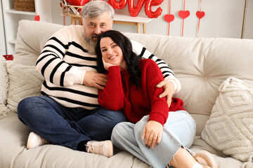 Obraz premium Beautiful mature couple sitting on sofa in decorated room. Valentine's Day celebration
