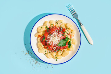 Plate of tasty gnocchi with tomato sauce and cheese on blue background