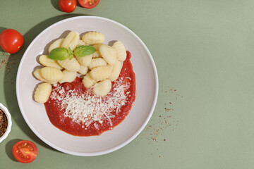 Plate of tasty gnocchi with tomato sauce and cheese on green background