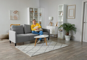 Young man with cushion sitting on grey sofa in living room
