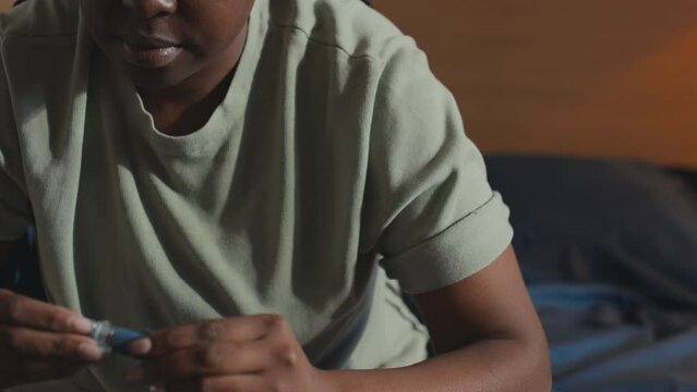 Close-up shot of young African American female with diabetes sitting on bed at home and injecting herself with insulin pen in upper arm and closing it