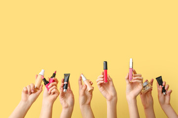 Female hands with lipsticks, glitters and foundation on yellow background