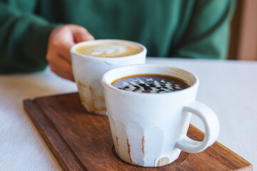 Closeup image of a woman holding and drinking coffee with friend in cafe