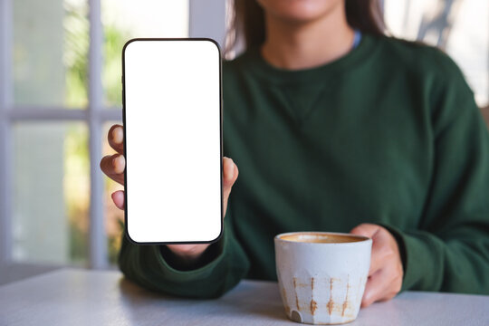 Mockup image of a woman holding and showing a mobile phone with blank white screen while drinking coffee