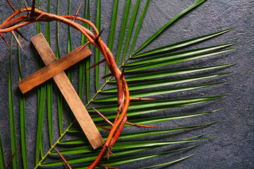 Wooden cross with crown of thorns and palm leaf on black background