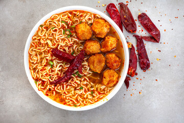 spicy instant noodles or ramen with fish balls and dried chili on mottled grey backdrop with copy...