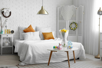 Interior of light bedroom decorated for Easter with bed and tulips in vase