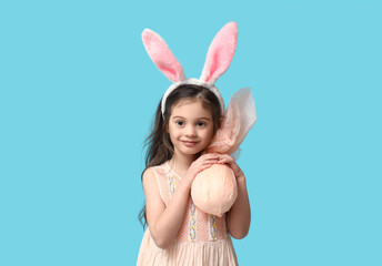 Cute little girl in bunny ears with Easter gift egg on blue background