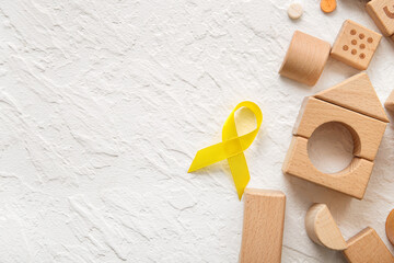 Golden ribbon with wooden toys and pills on white grunge background. Children cancer awareness concept