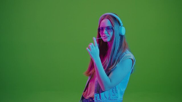 Green Screen. Teenage Girl Dancing In Neon Lights, Immersed In Music From Her Headphones, Chewing A Large Pink Bubblegum. A Fusion Of Retro Vibes With Modern Youth Culture And Passion For Music.