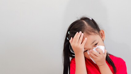 little Asian girl holding forehead feel sick and sneeze with tissue paper on gray background