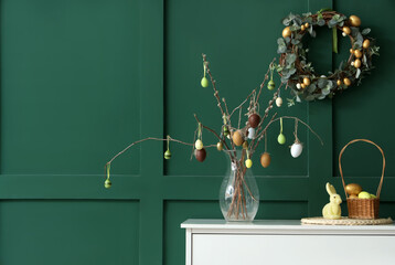 Vase with willow branches and Easter eggs on commode near green wall