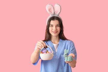 Female doctor in bunny ears with Easter rabbit and eggs on pink background