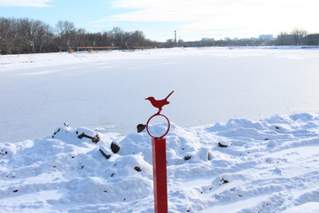 a lake in ice in winter and a red fence with a red bird
